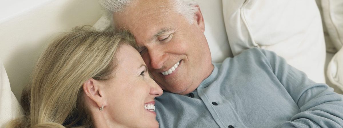 Smiling older couple lying close together on a couch, heads touching affectionately.