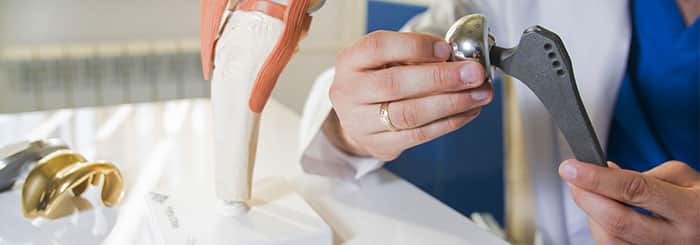 natural-alternative-to-hip-replacement Medical professional in blue scrubs adjusting a knee joint prosthesis on a leg model.