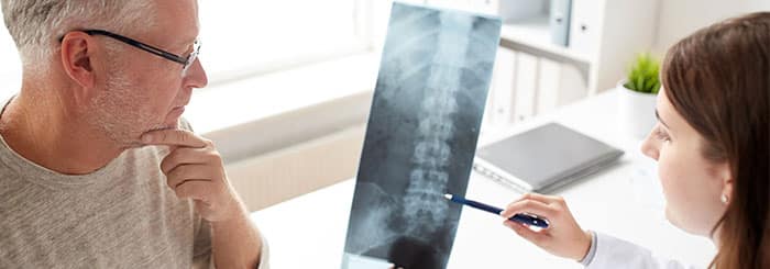 Medical professional shows a spinal X-ray to an older man during a consultation in a bright clinic.