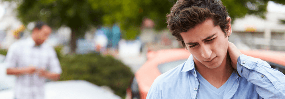 Young man in a light blue shirt gazes downward, hand resting on his neck, appearing stressed as others in the blurred background go about their day