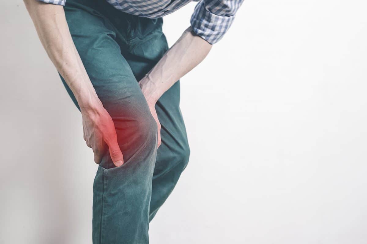 Person holding their knee in visible pain, with a red glow at the knee to indicate injury or soreness.