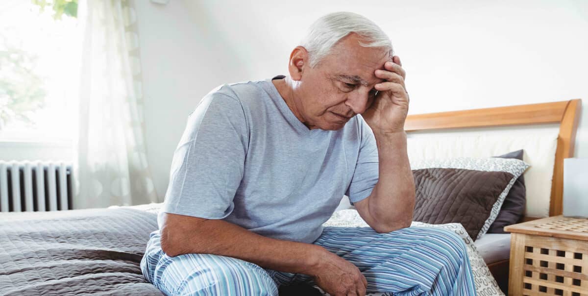 cells6-pdf-1-1200×604 Older man sits on a bed, hand on his forehead, looking distressed in a sunlit bedroom.