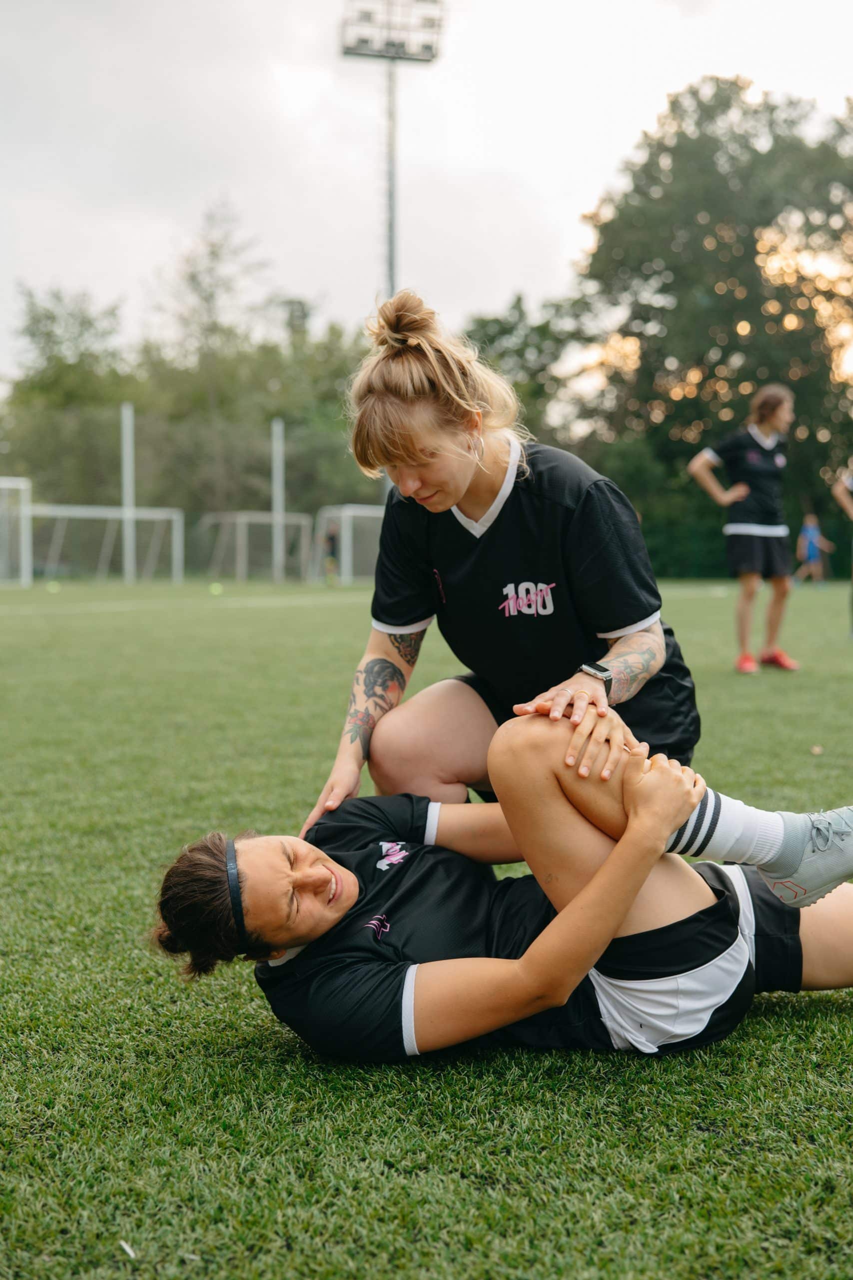 Two players wearing black uniforms grapple on a grassy field during a game or training drill.
