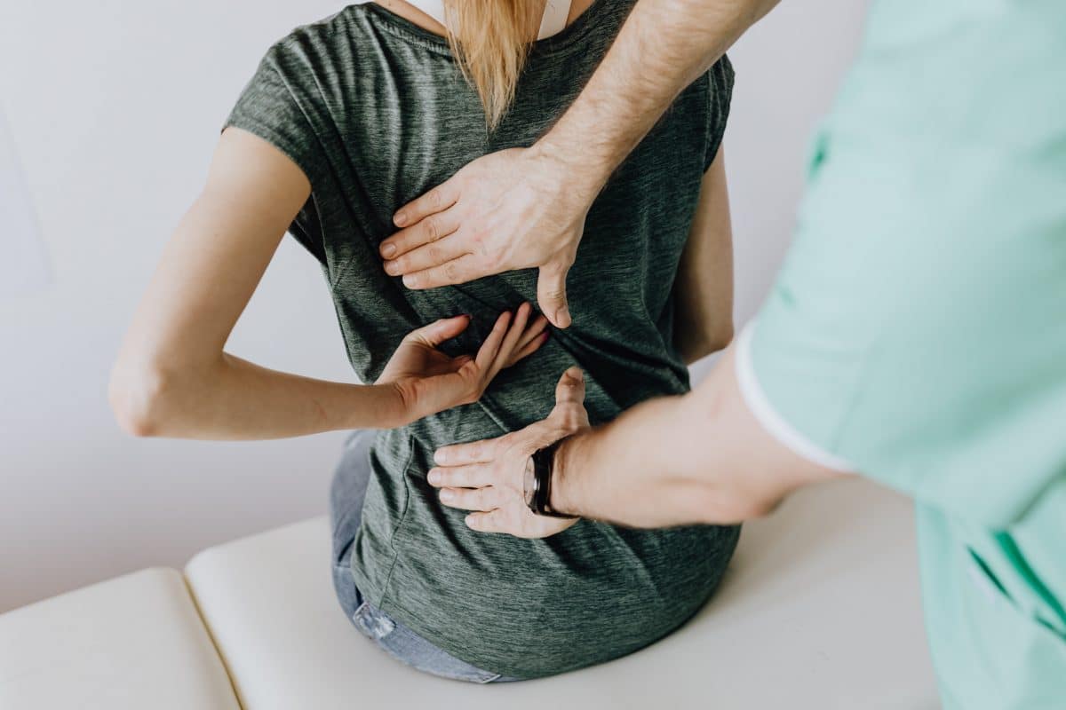 Clinician placing hands on a person's back during a spine examination in a green shirt.