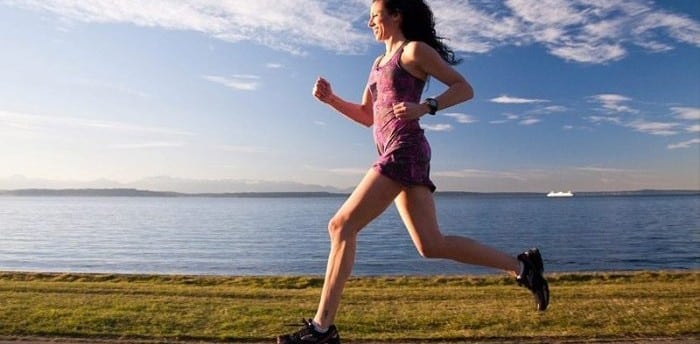 Woman running along a lakeside path under a blue sky.