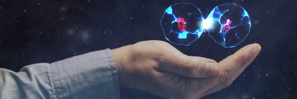Hand beneath a starry background holds two glowing blue cells connected by a bright link, symbolizing biotechnology and genetics.
